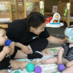 Intern Kyanna engages with two infants and playing with purple, blue, and green balls