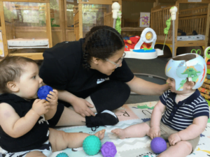 Intern Kyanna engages with two infants and playing with purple, blue, and green balls